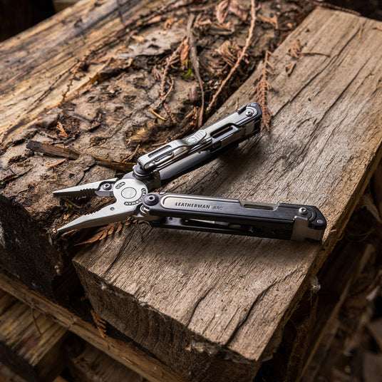 Translation missing: en.An open Leatherman Arc, showcasing it's pliers and pocket clip, lies atop a piece of wood, emphasizing it's utility and craftsmanship