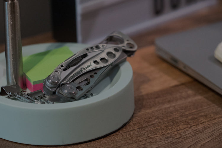 Translation missing: en.Stainless Steel Leatherman Skeletool® resting on a desk organizer beside a notebook and sticky notes in a modern workspace.