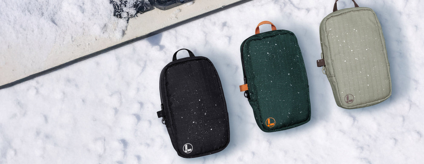 Translation missing: en.Black, hunter green, and mossy fog Leatherman tool pouches on a snowy background with a snowboard