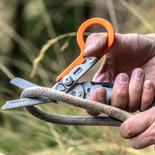 Translation missing: en. A man using an orange and black Leatherman Raptor Rescue shears to cut a thick rope