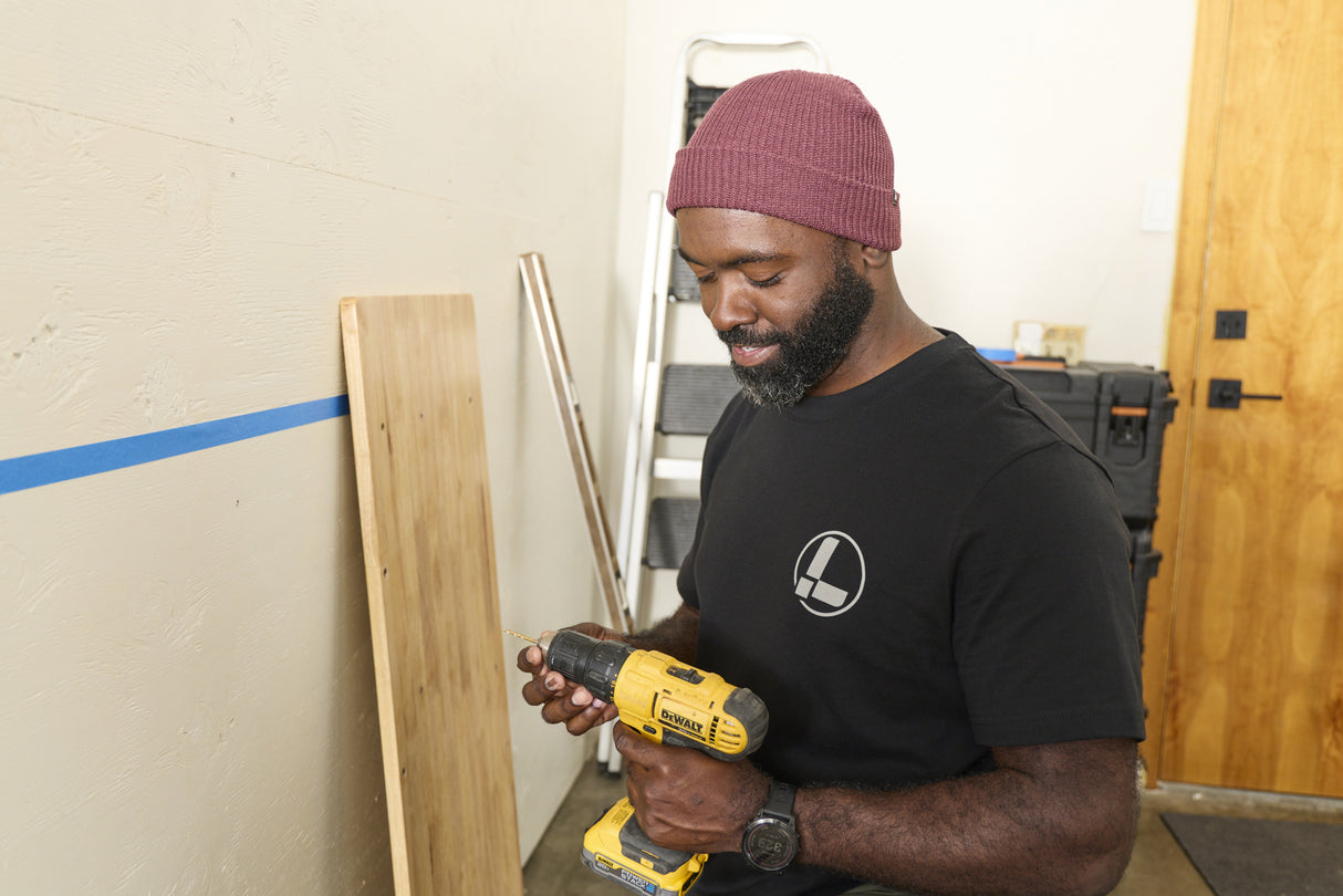 Translation missing: en.A person wearing a black Leatherman Classic Tee holding a yellow power drill while working indoors