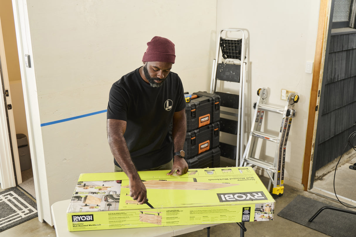 Translation missing: en.A person wearing a black Leatherman Classic Tee using the blade on a Leatherman multi-tool to open a large box that is laying on top of a folding table