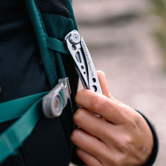 Translation missing: en.Person holding a closed Skeletool KBX that is attached to the strap of a backpack