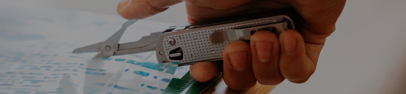 Translation missing: en.Hand holding Leatherman Free T2 with scissors opened, being used to cut paper.