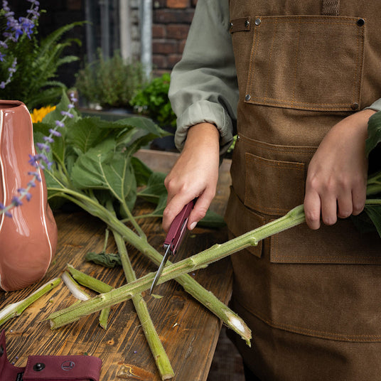 Translation missing: en.Woman using the knife on a Heathered Cranberry Leatherman Bond to cut the bottom of a sunflower stem
