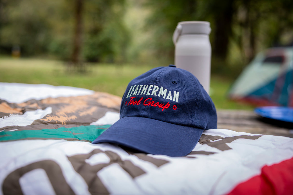 Translation missing: en.A navy blue Leatherman Dad Hat resting on a blanket outdoors at a campsite, with a white bottle and tent blurred in the background