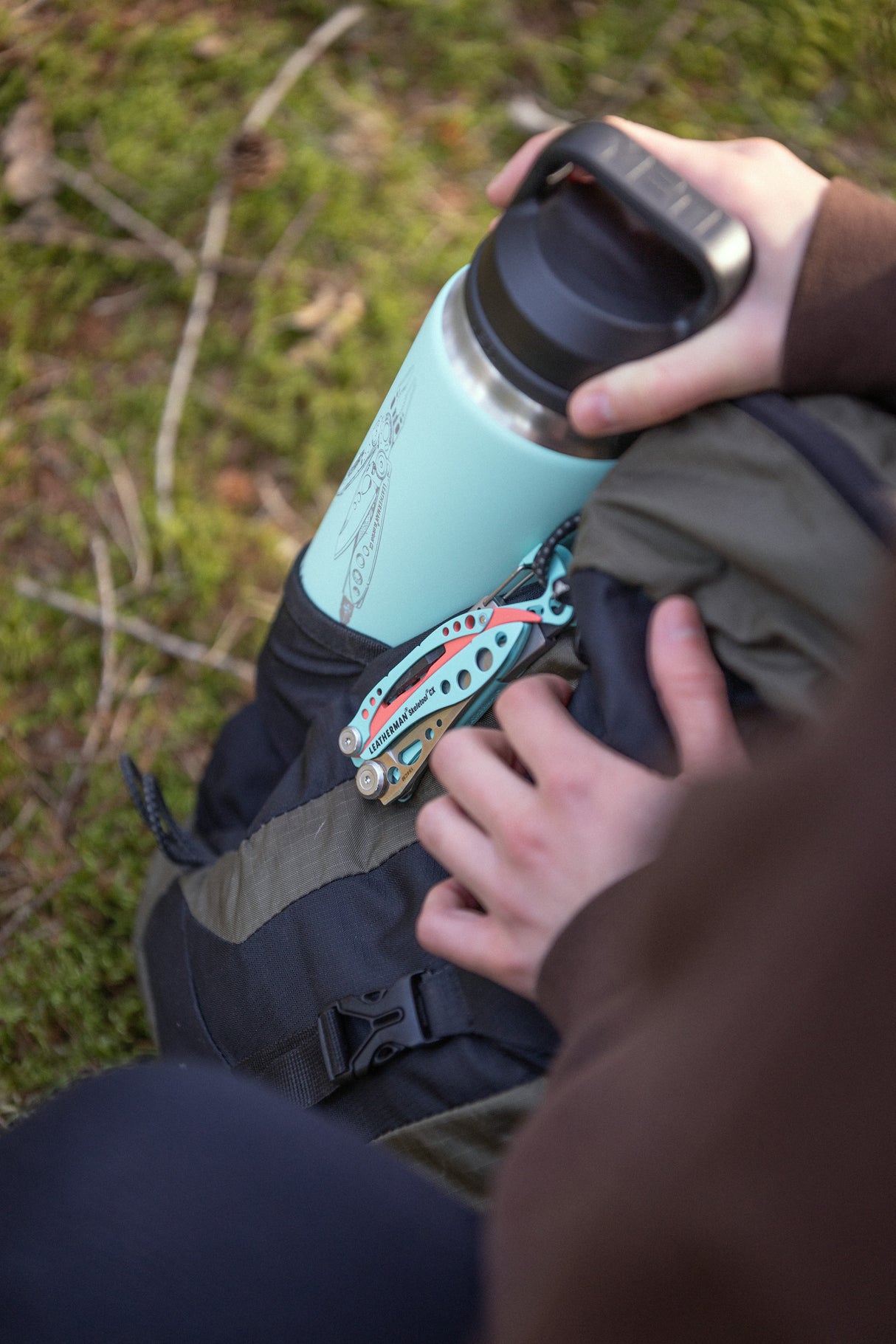 Translation missing: en.Hand holding a mint green Yeti bottle in a backpack pocket with a Paradise Leatherman Skeletool CX multitool clipped on