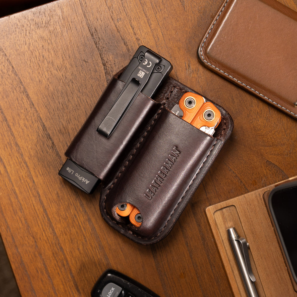 Translation missing: en.Dark Brown Premium Leather Sheath holding a black flashlight and orange multitool on a wooden desk