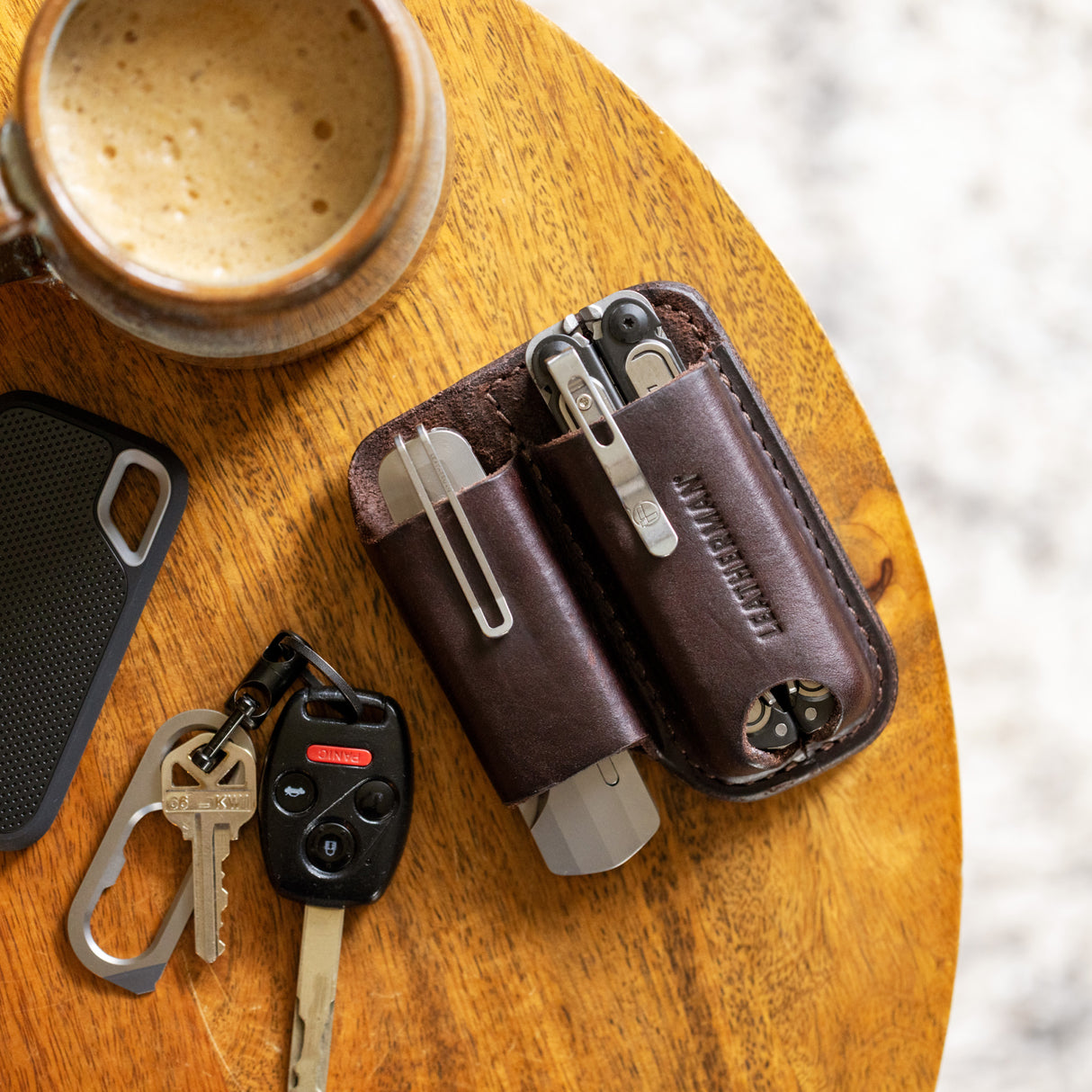 Translation missing: en.Dark Brown Premium Leather Sheath on a table beside keys, phone case, and a mug of coffee