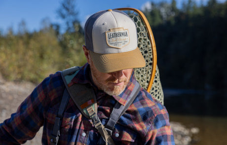 Translation missing: en.Man wearing a Leatherman Pacific Northwest Trucker hat walking alongside a stream carrying a backpack and net