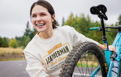 Translation missing: en.Woman wearing a Leatherman Pacific Northwest crewneck, standing next to a bicycle outdoors