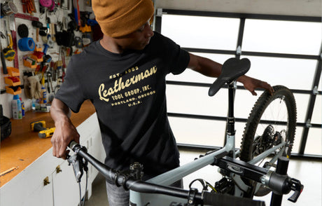 Translation missing: en.Person assembling a bicycle in a workshop wearing a black Leatherman Vintage Tee