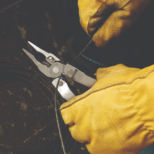 Translation missing: en. A person wearing yellow leather gloves using a Leatherman Rebar to cut wire