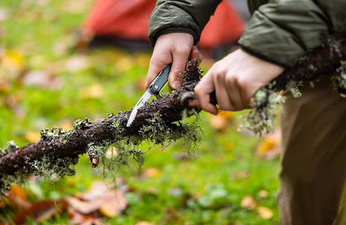Translation missing: en.Person using a Mossy Slate Leatherman Rebar saw on a moss-covered branch outdoors