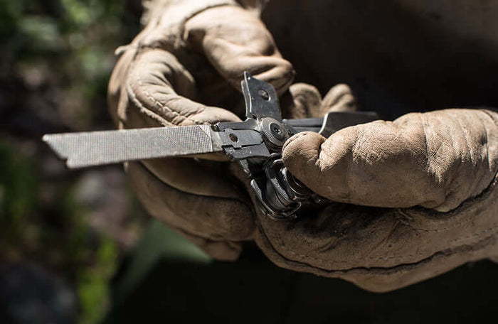 Translation missing: en.Close-up of hands in gloves holding a Leatherman Surge® multitool with a file attachment