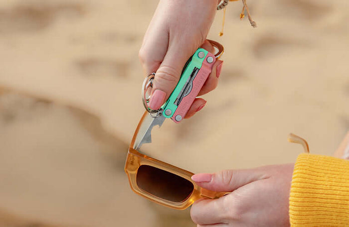 Translation missing: en.Person using the extra small screwdriver on a Leatherman Micra® in Bayside color to tighten sunglasses on the beach