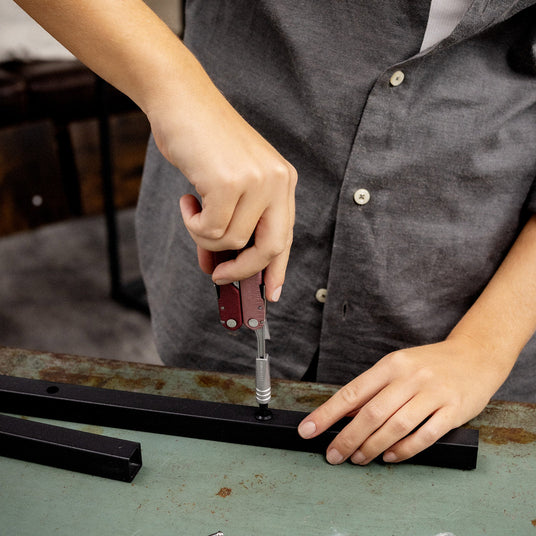 Woman using a Leatherman Heathered Cranberry Rebar with an extender attached to screw something into a metal pole.