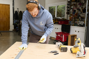 Translation missing: en.A person wearing a Storm Blue Leatherman Classic Hoodie measuring a wooden board in a workshop