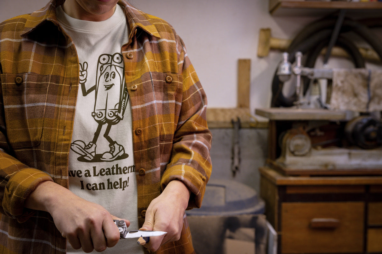 Translation missing: en.A person wearing a natural-colored Leatherman Mr. Wave Tee with a cartoon multitool design using a Leatherman multitool to sharpen a pencil