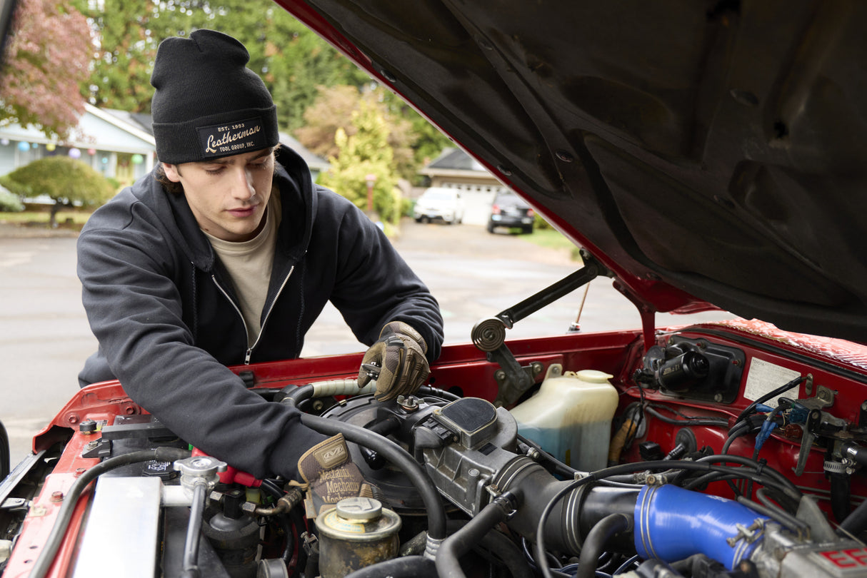 Translation missing: en.A person wearing a black Leatherman Vintage Beanie working under the hood of a red vehicle in a residential driveway
