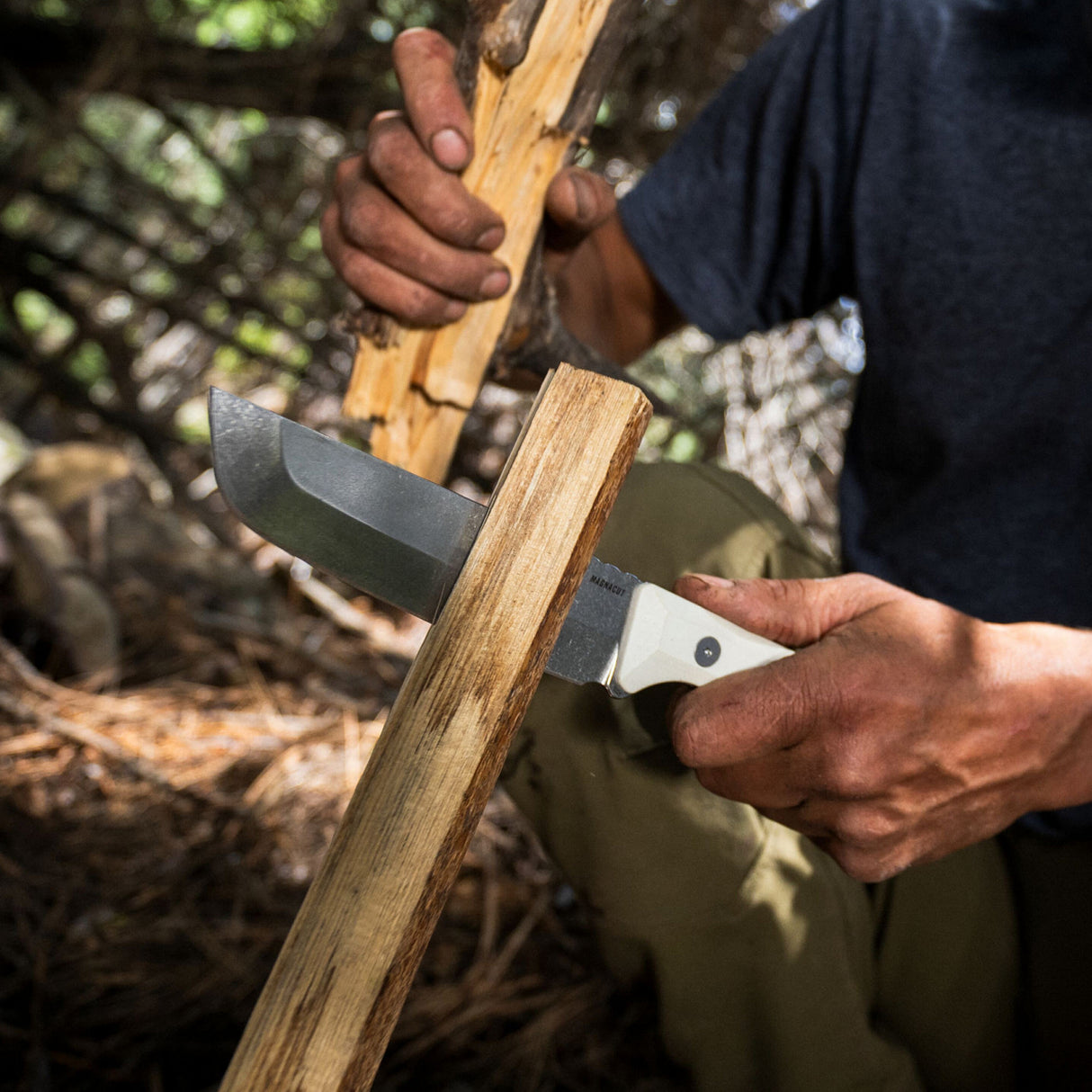 Translation missing: en.A man skillfully uses a Leatherman Alpine Pioneer knife to slice through a wooden plank, demonstrating craftsmanship in a workshop environment