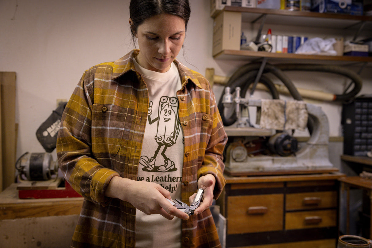 Translation missing: en.A person wearing a natural-colored Leatherman Mr. Wave Tee with a cartoon multitool design opening a Leatherman multitool in a garage