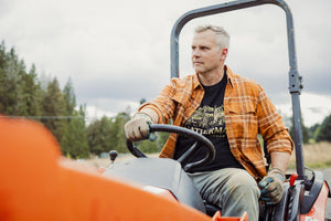 Translation missing: en.A person wearing a black Leatherman Timber Tee driving a tractor outdoors