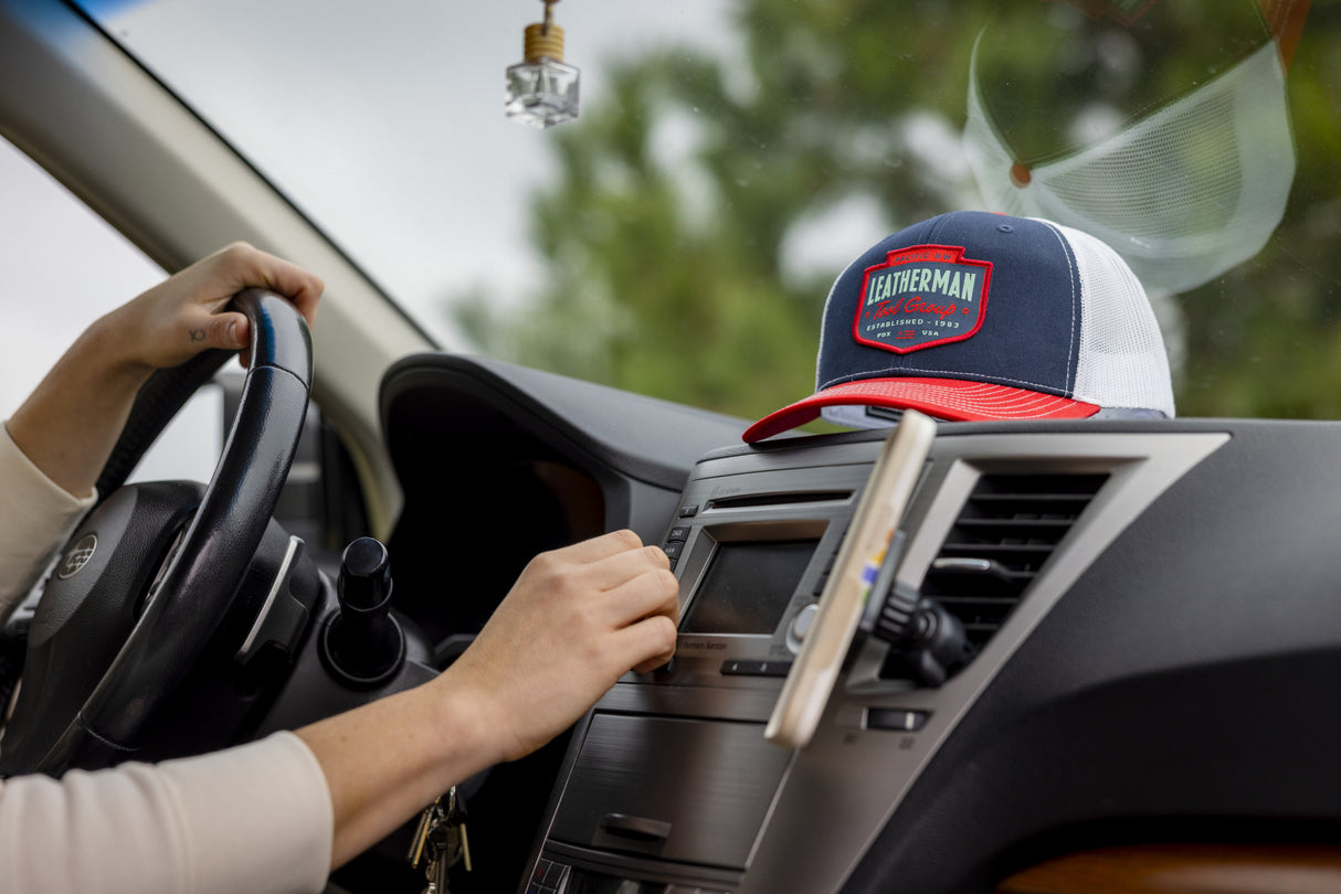 Translation missing: en.A person in a car with a navy Leatherman PNW Trucker Hat with a white mesh back and red brim resting on the dashboard