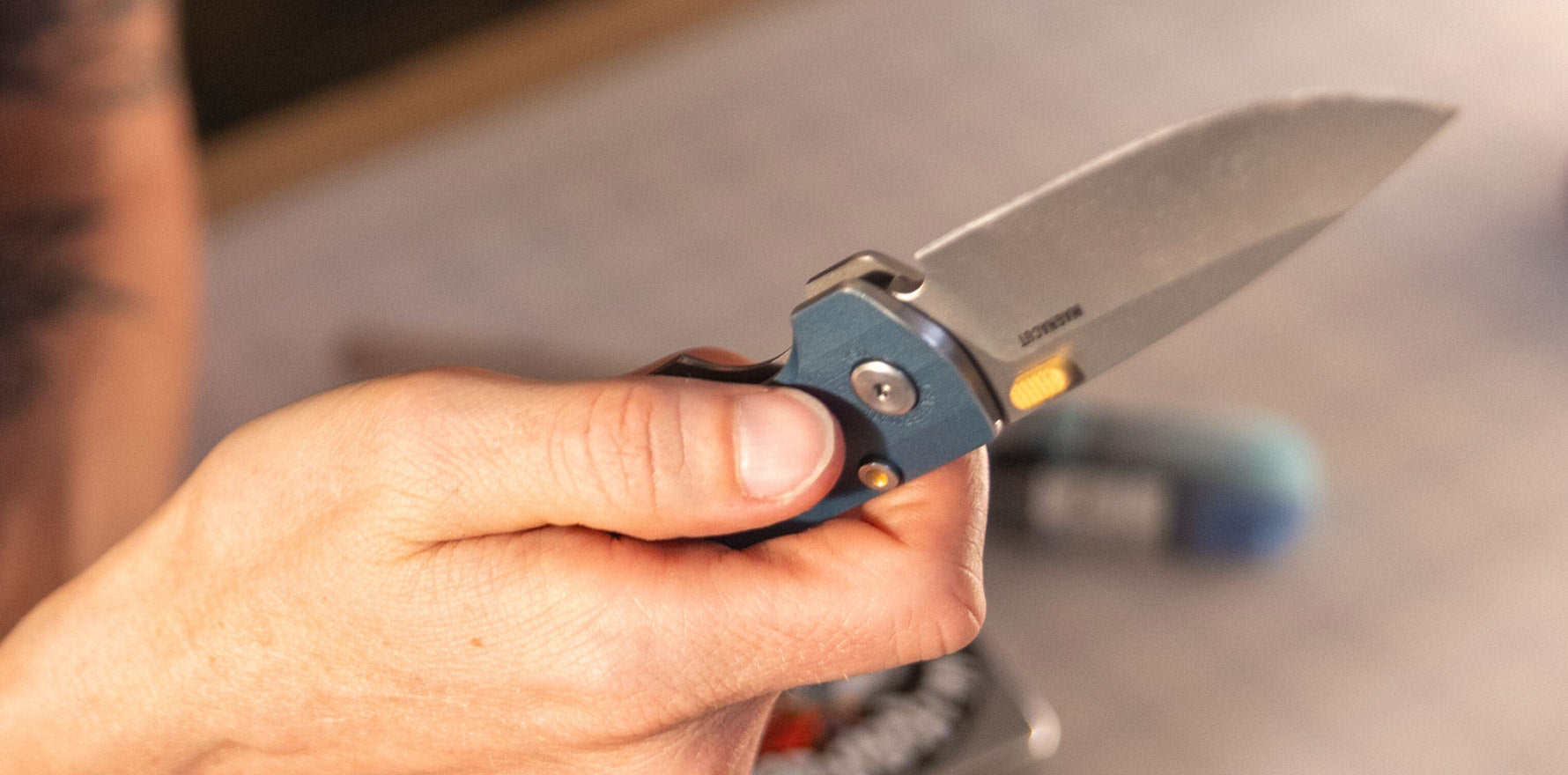 Person holding a Leatherman Blazer Denim folding knife in an open position, with focus on the hand grip and blade detail in a casual indoor setting.