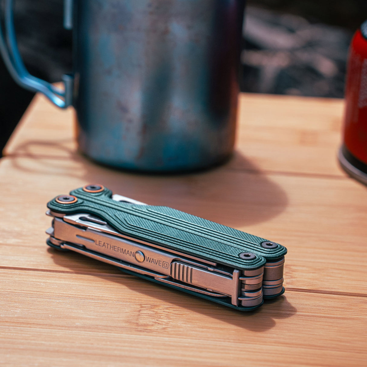 Translation missing: en.Cascadia Leatherman Wave® Alpha multitool on a wooden surface with camping gear in the background