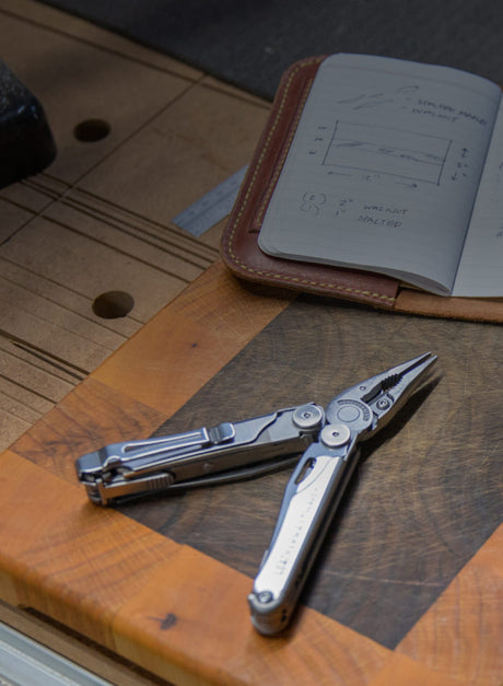 Leatherman Wave Plus multi-tool on a workbench table with a notebook