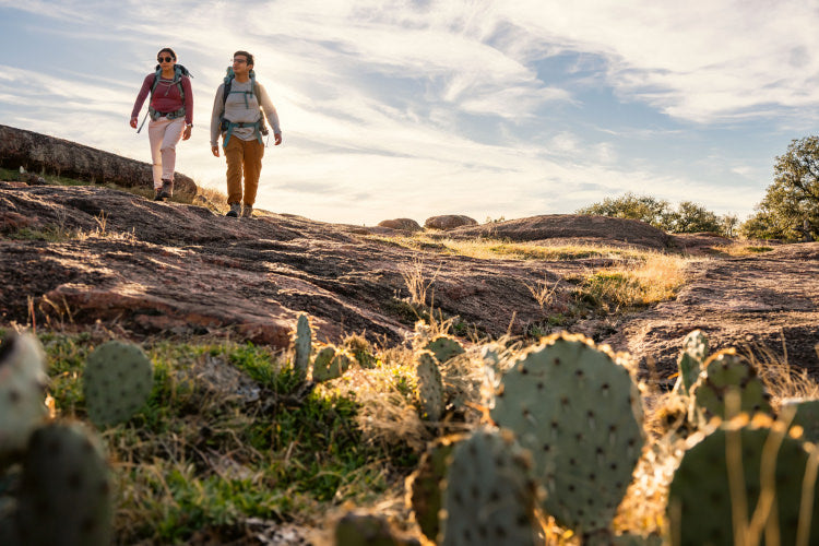 Two hikers wearing backpacks walking through a field