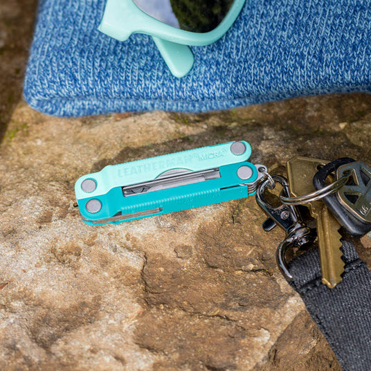 Translation missing: en.Leatherman Parakeet Micra® multitool on a rock next to sunglasses and keys, showcasing its compact design