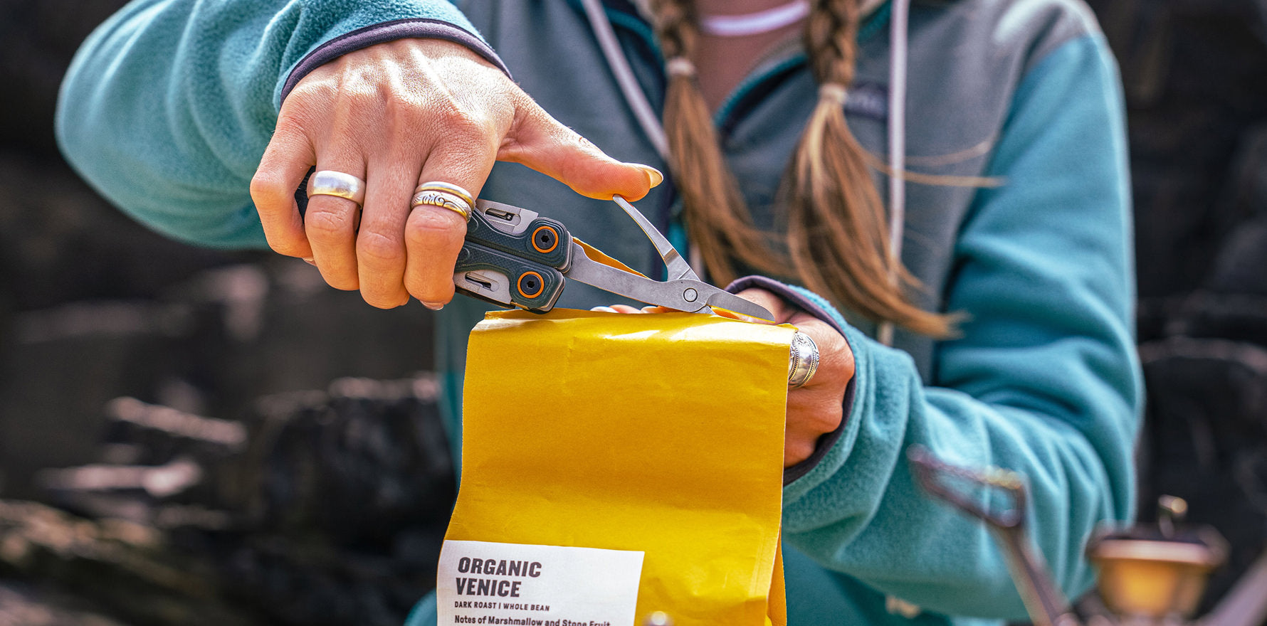 Person using the scissors on the Leatherman Wave® Alpha Cascadia multi-tool to cut open a yellow bag of organic coffee beans.
