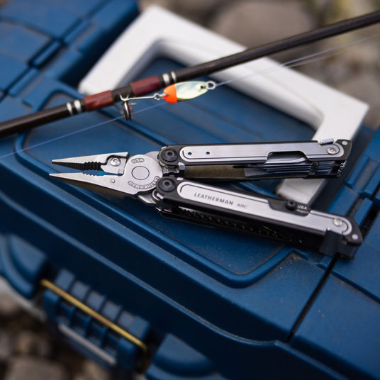 Opened Leatherman Arc and fishing rod on top of blue fishing box.