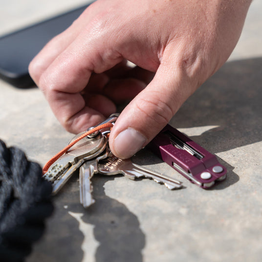 Person holding cherry Leatherman Micra on keyring next to mobile phone. 