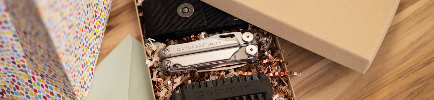 Leatherman Wave closed in a gift box next to a sheath and a bit kit on a table