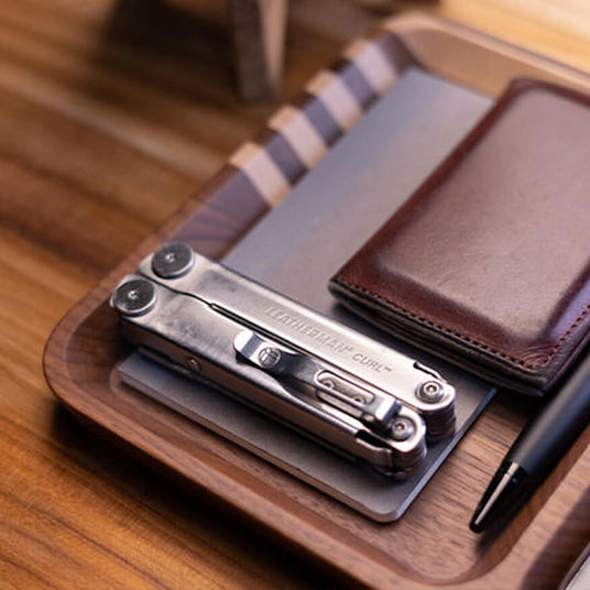 Leatherman Curl on top of gray notebook next to brown leather wallet and black pen. 