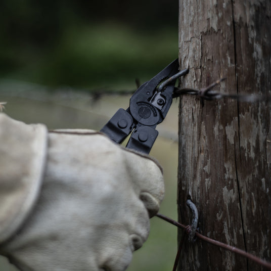 Person with gloves using a black Super Tool 300 pliers to cut a wire.