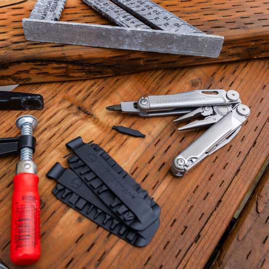 Various tools laid out on a wooden surface including Leatherman Wave multi-tool, screwdriver, and metal ruler.