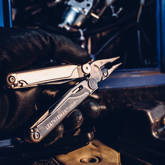 A person’s hand wearing a black glove holding a Leatherman Wave multitool with pliers extended