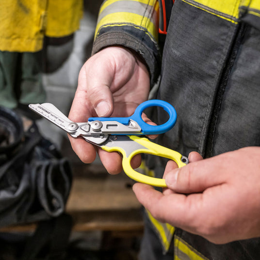 Firefighter holding opened Leatherman blue and yellow Raptor shears. 