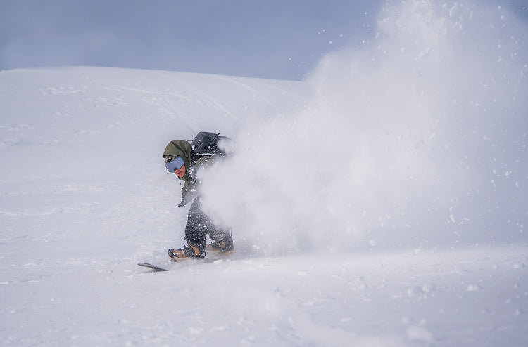 Translation missing: en.Person snowboarding in deep powder snow with a blue sky background