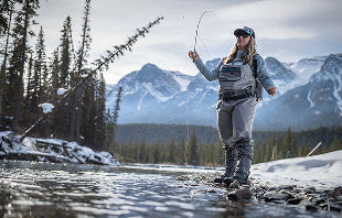 Translation missing: en.A woman stands in shallow water, casting a fly rod, surrounded by nature and reflecting a peaceful fishing scene