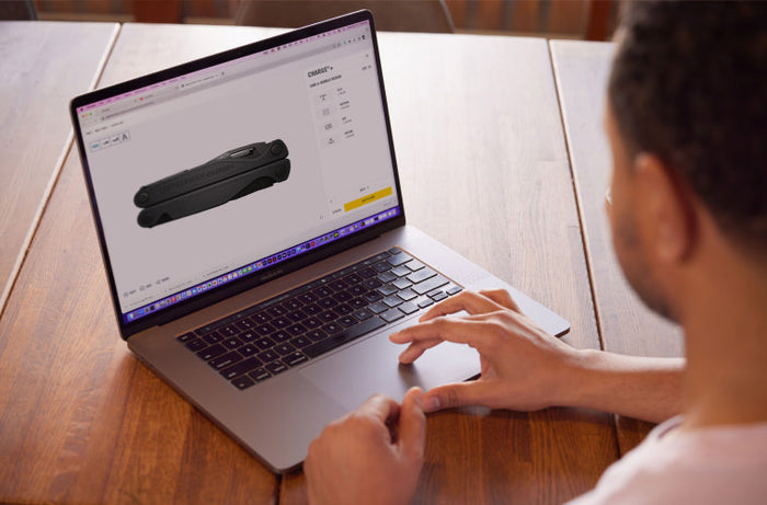 Translation missing: en.Person browsing a laptop showing product details on a wooden table
