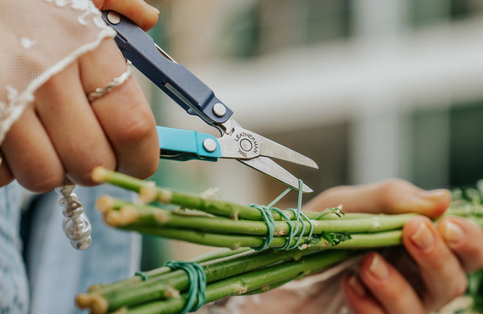 Translation missing: en.Person using the scissors on a Leatherman Micra® in Lavender Mist color to cut the rubber band holding flower stems