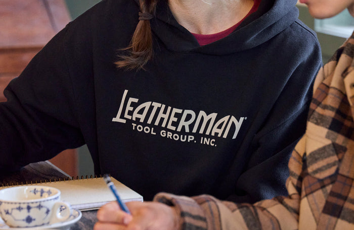 Translation missing: en.Person wearing a Leatherman Tool Group hoodie while taking notes at a table with a cup of coffee