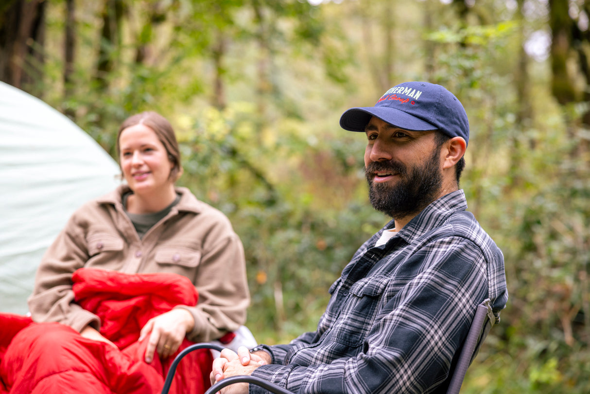 Translation missing: en.A man and woman sitting outdoors near a tent. The man is wearing a navy Leatherman Dad hat