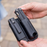 Translation missing: en.Hands holding a black leather sheath carrying two black multitools outdoors