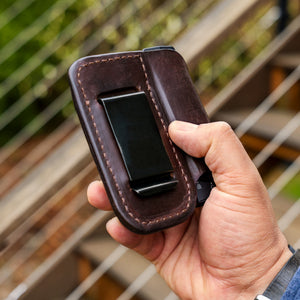Translation missing: en.Hand holding a Dark Brown Premium Leather Sheath with a black metal clip outdoors